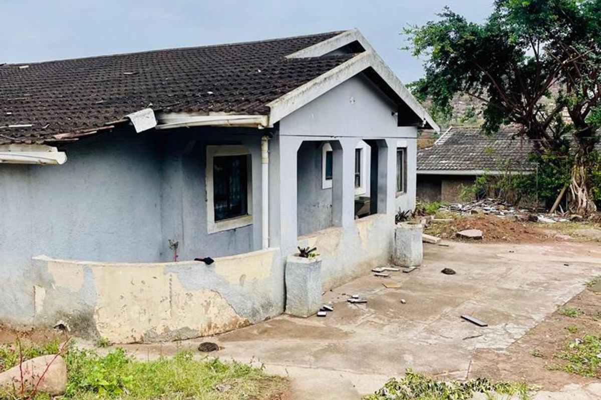 Rear view of a detached house showing a concrete patio area, tiled roof, and exterior walls requiring significant maintenance and repair.