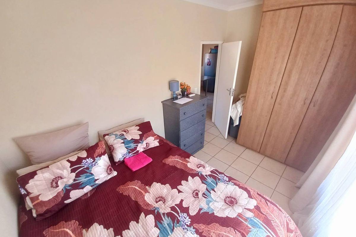 A bedroom featuring built-in wooden wardrobes and tiled flooring, with an adjacent doorway leading to another room.