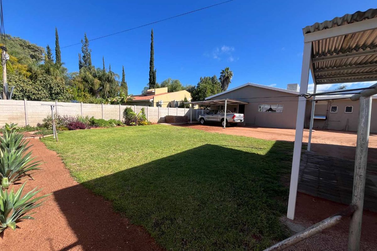 Spacious rear garden featuring a well-maintained lawn, perimeter walling, and a covered carport area providing convenient off-street parking.