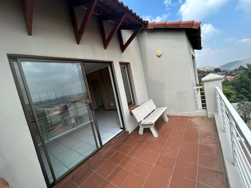 A spacious balcony featuring terracotta tiling, metal railings, and sliding door access, offering elevated views of the surrounding area.