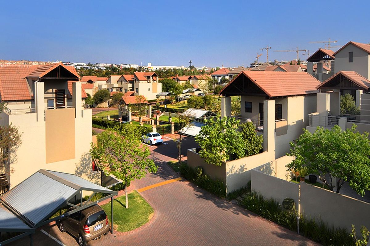An elevated view of a residential apartment complex featuring paved driveways, covered parking structures, and landscaped garden areas.