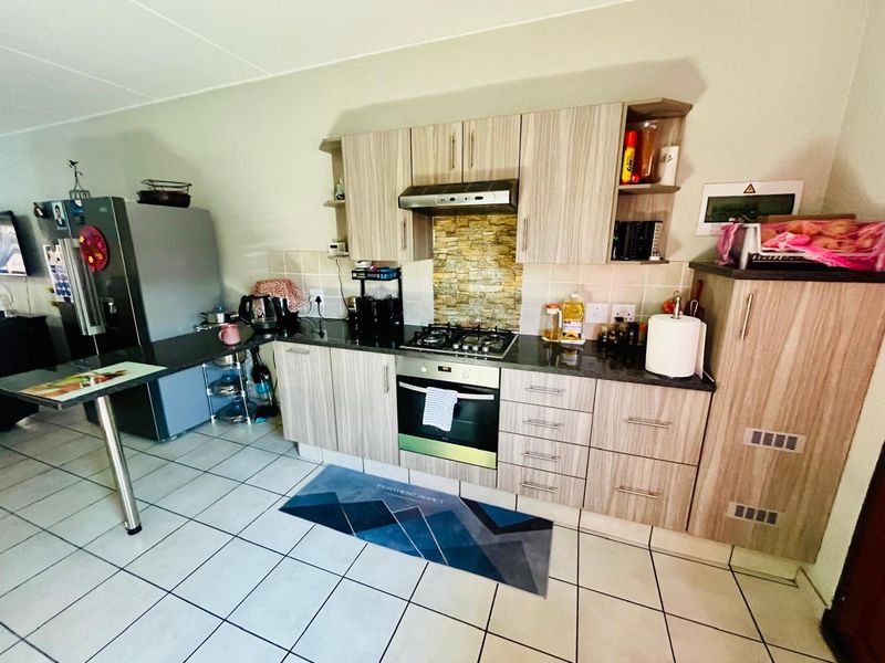 A functional kitchen featuring wood-look cabinetry, stone countertops, a gas hob, and an integrated oven with tiled splashback and flooring.