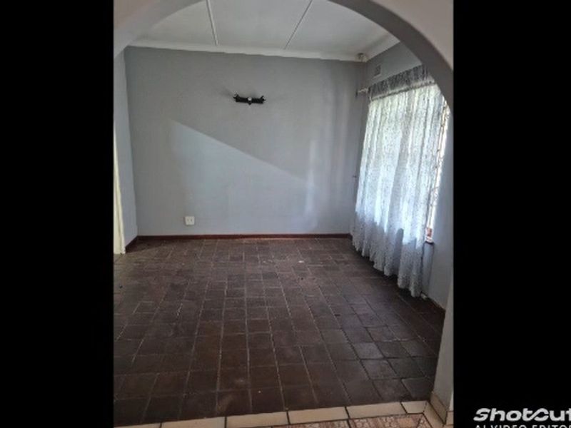 An empty living room featuring a classic archway entrance, dark tiled flooring, and a neutral wall finish, ready for renovation or staging.
