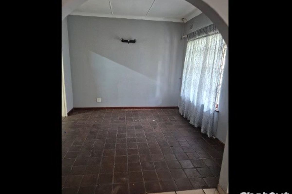 An empty living room featuring a classic archway entrance, dark tiled flooring, and a neutral wall finish, ready for renovation or staging.