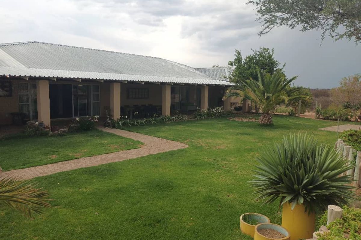 A view of the rear exterior of the property, featuring a covered patio area, a well-maintained lawn, and established garden landscaping.