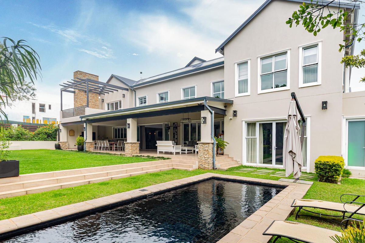 Spacious rear exterior featuring a covered patio, landscaped garden, and a modern swimming pool with stone-clad pillars and architectural detailing.
