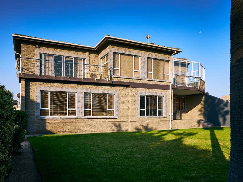 Rear view of a two-story brick house featuring a spacious lawn, upper-level balconies with metal railings, and large windows.
