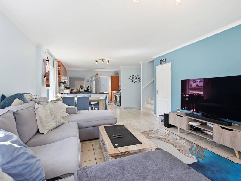 Open-plan living area featuring tiled flooring, a connected kitchen space, and a staircase leading to the upper level.