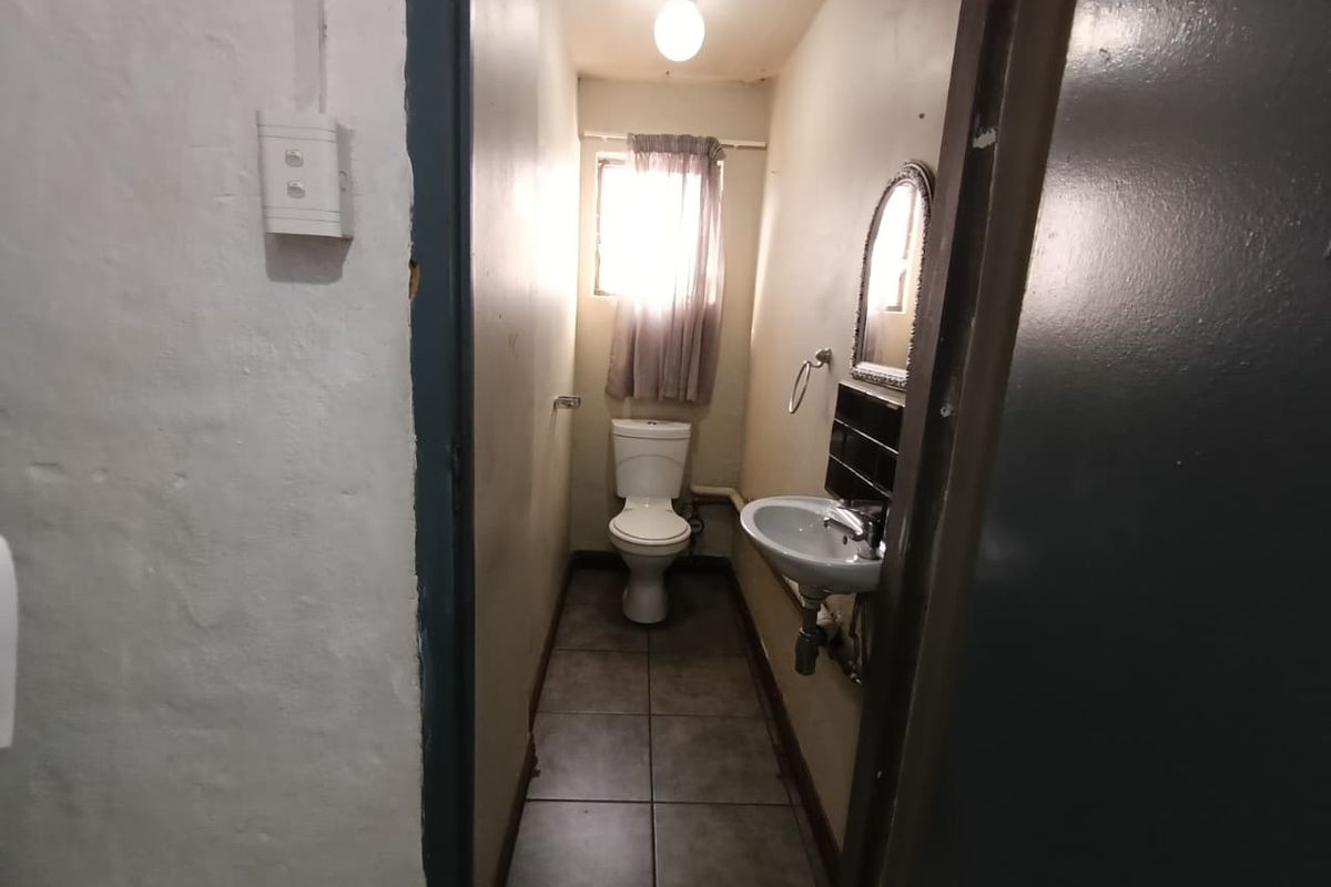 A compact industrial-style bathroom featuring a pedestal basin, toilet, and tiled flooring, requiring cosmetic updates to improve its overall condition.