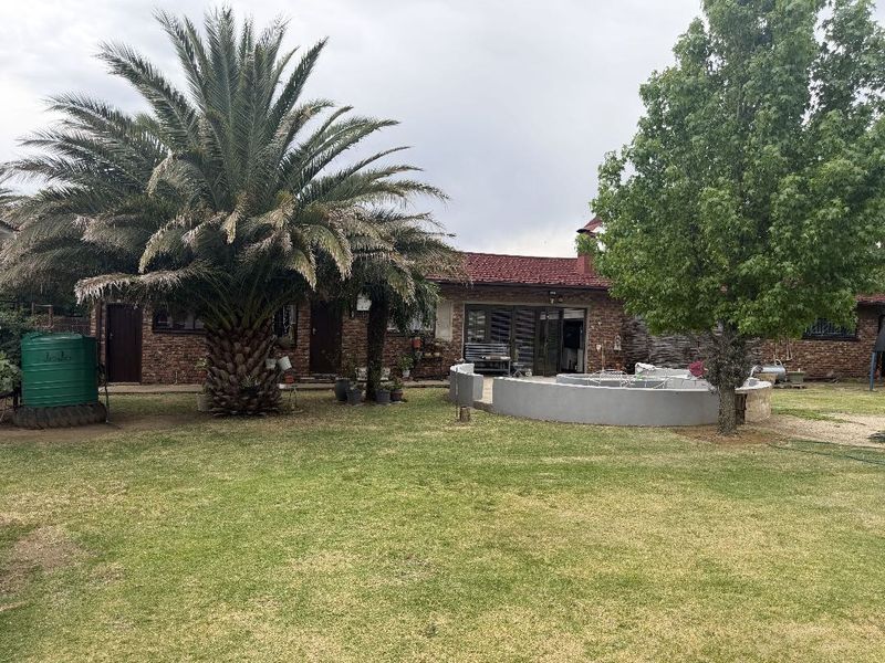 Rear view of the property featuring a brick facade, tiled roof, and a curved masonry wall set within a spacious garden area.