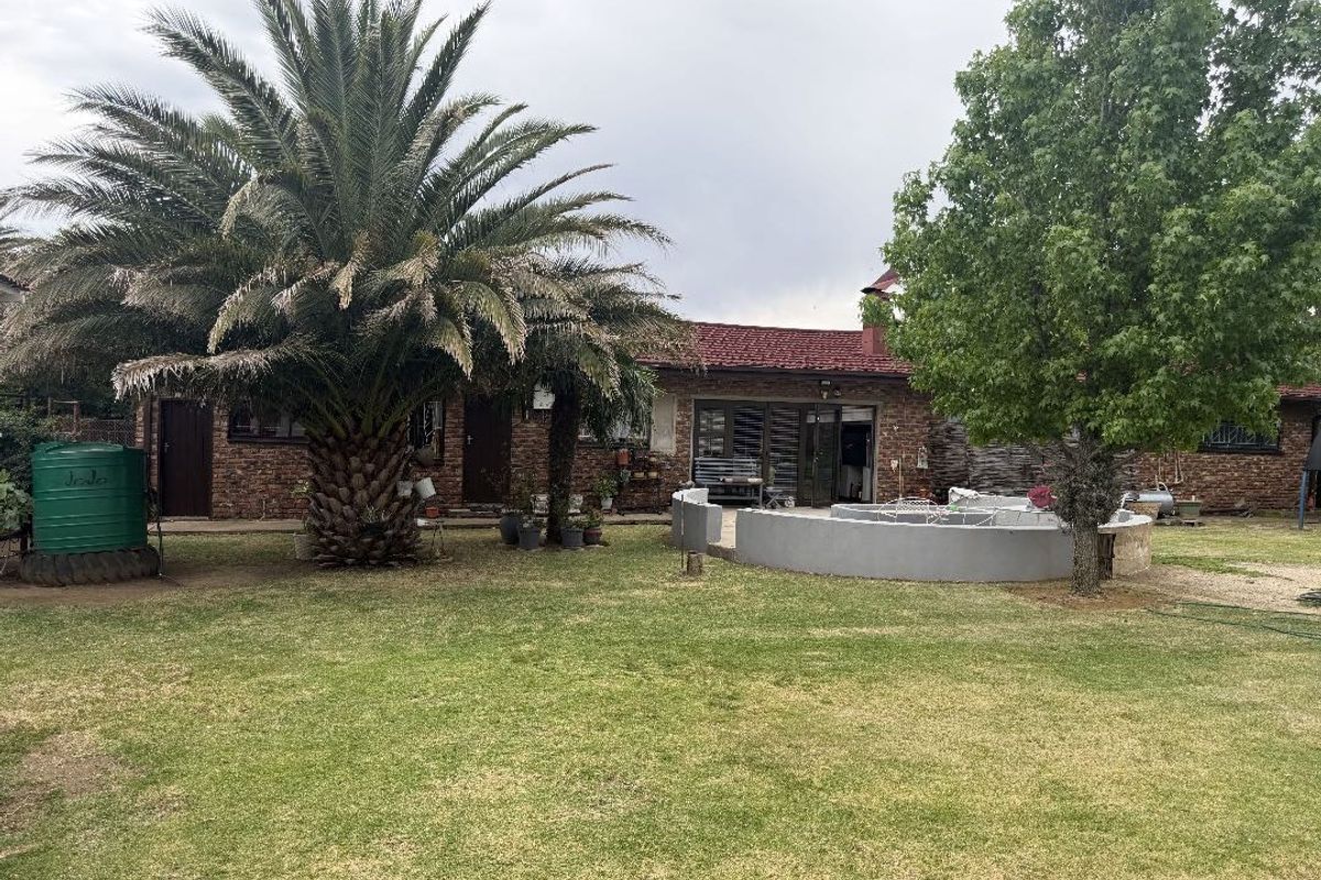 Rear view of the property featuring a brick facade, tiled roof, and a curved masonry wall set within a spacious garden area.