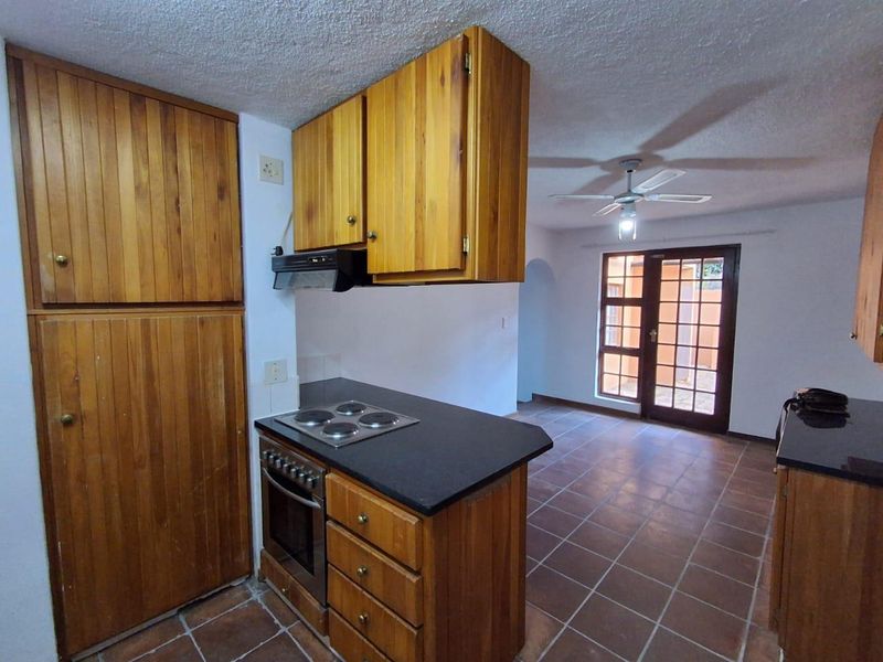 Open plan kitchen and living area featuring wooden cabinetry, built-in oven, hob, extractor fan, tiled flooring, and access to the exterior via french doors.