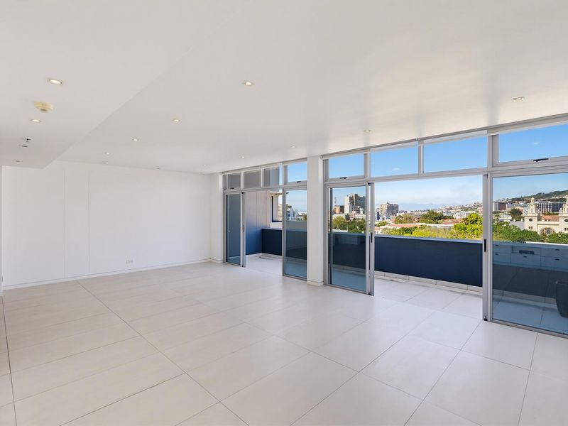 Spacious, light-filled living area featuring large format floor tiles, recessed lighting, and expansive sliding glass doors opening onto a private balcony with city views.