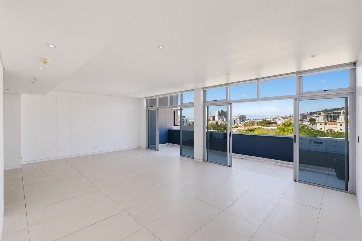 Spacious, light-filled living area featuring large format floor tiles, recessed lighting, and expansive sliding glass doors opening onto a private balcony with city views.