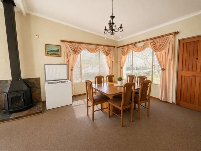 A dining room featuring a freestanding fireplace with a tiled hearth, coved ceilings, and large windows with traditional drapery.