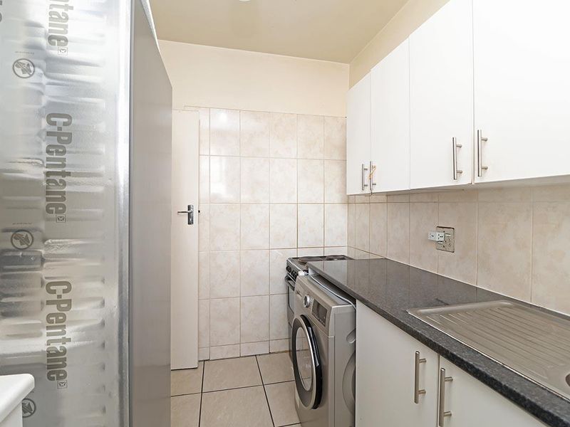 Compact kitchen featuring white cabinetry, granite countertops, tiled backsplash, and integrated sink, providing a functional and efficient workspace.