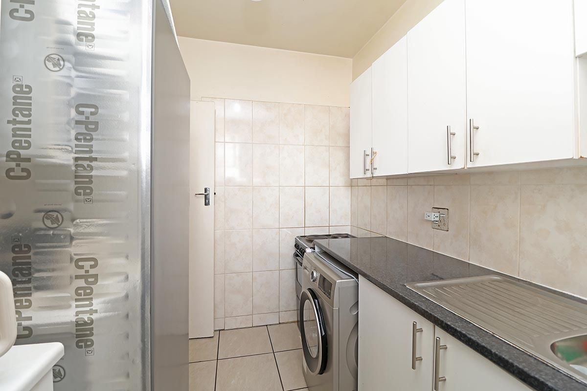 Compact kitchen featuring white cabinetry, granite countertops, tiled backsplash, and integrated sink, providing a functional and efficient workspace.
