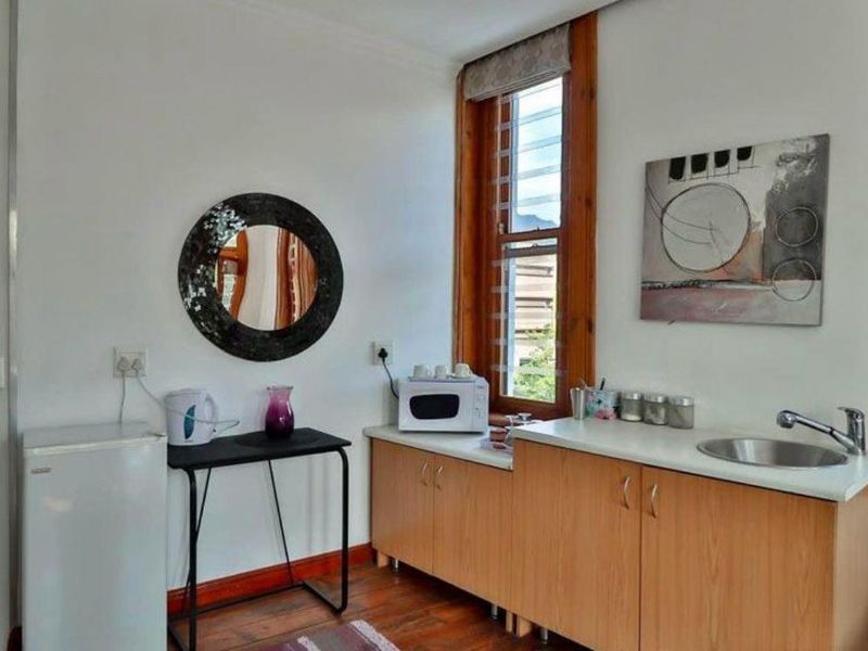 A compact kitchenette featuring wooden cabinetry, a stainless steel sink, and timber window frames, providing functional preparation space.