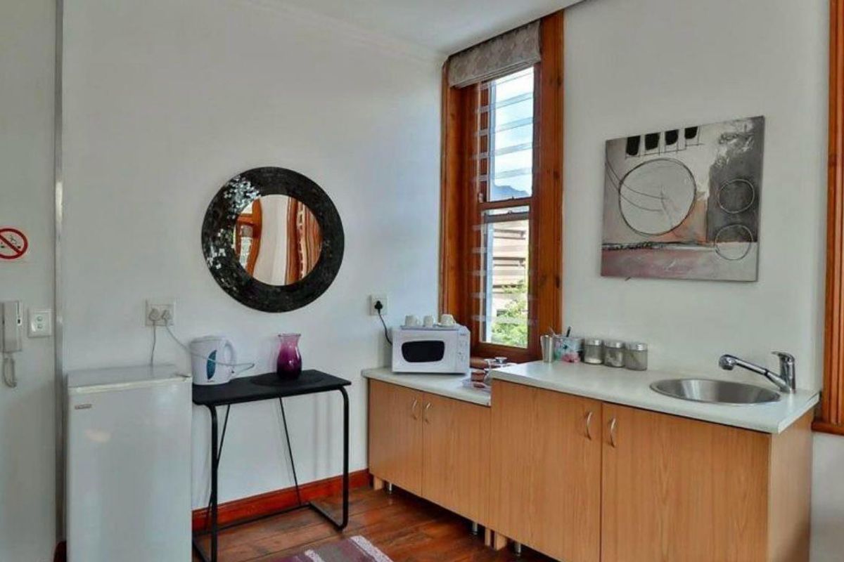 A compact kitchenette featuring wooden cabinetry, a stainless steel sink, and timber window frames, providing functional preparation space.