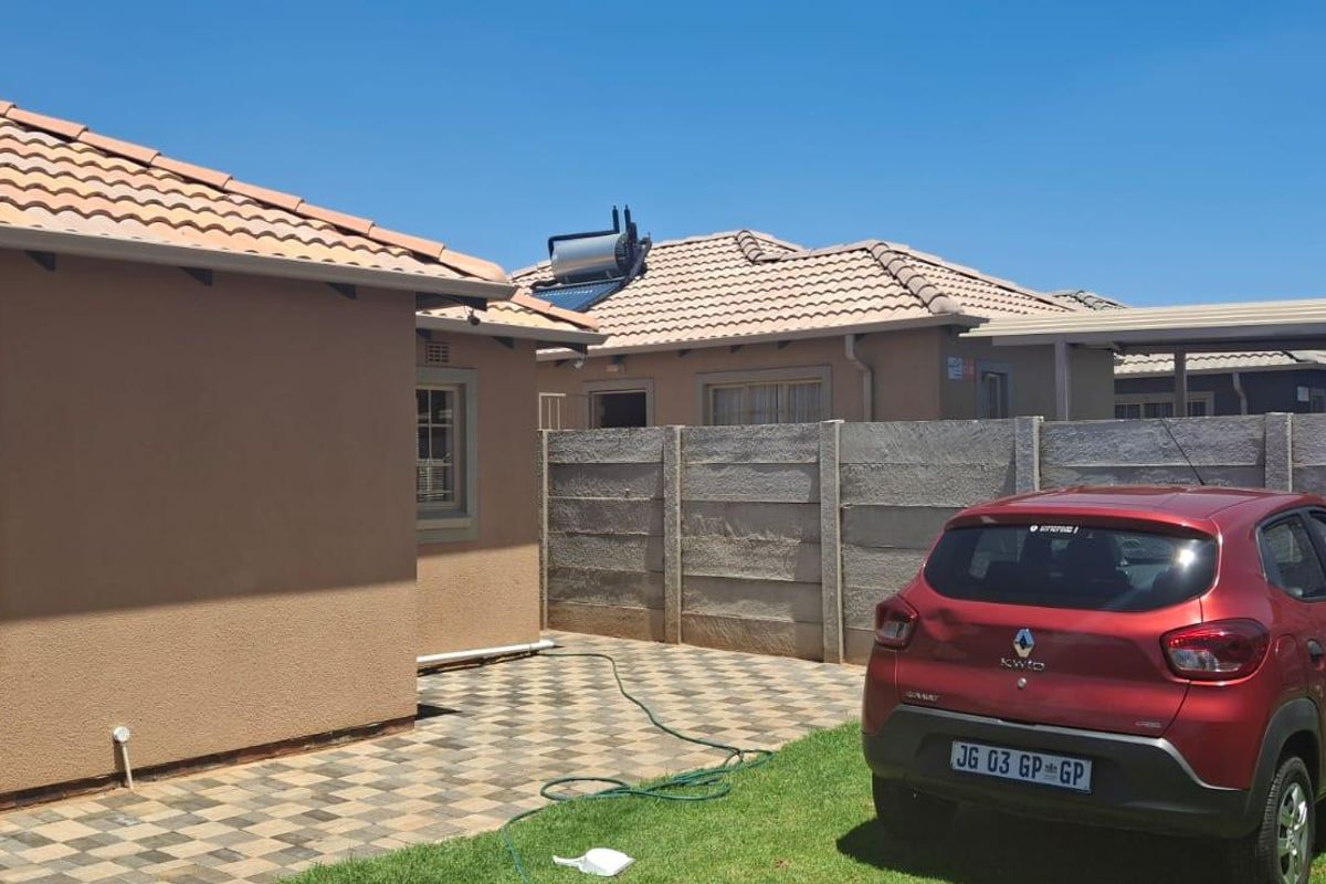 Exterior view of the property featuring a paved driveway, tiled roof, solar water heater, and perimeter precast concrete walling.