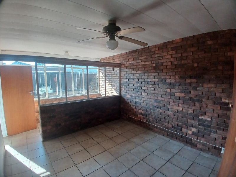 An enclosed patio area featuring exposed brick walls, tiled flooring, and a ceiling fan, offering a versatile space with large windows.