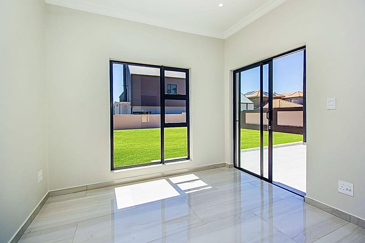 A bright, modern living area featuring large black-framed windows and sliding glass doors that open onto a private garden and patio.
