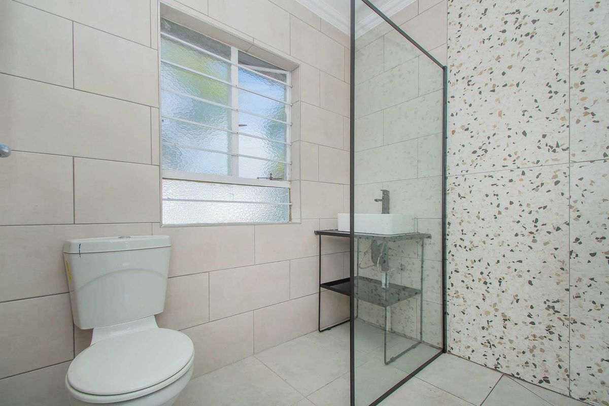 Modern bathroom featuring a glass-enclosed shower, terrazzo-style accent tiling, a contemporary vessel sink vanity, and a standard toilet.