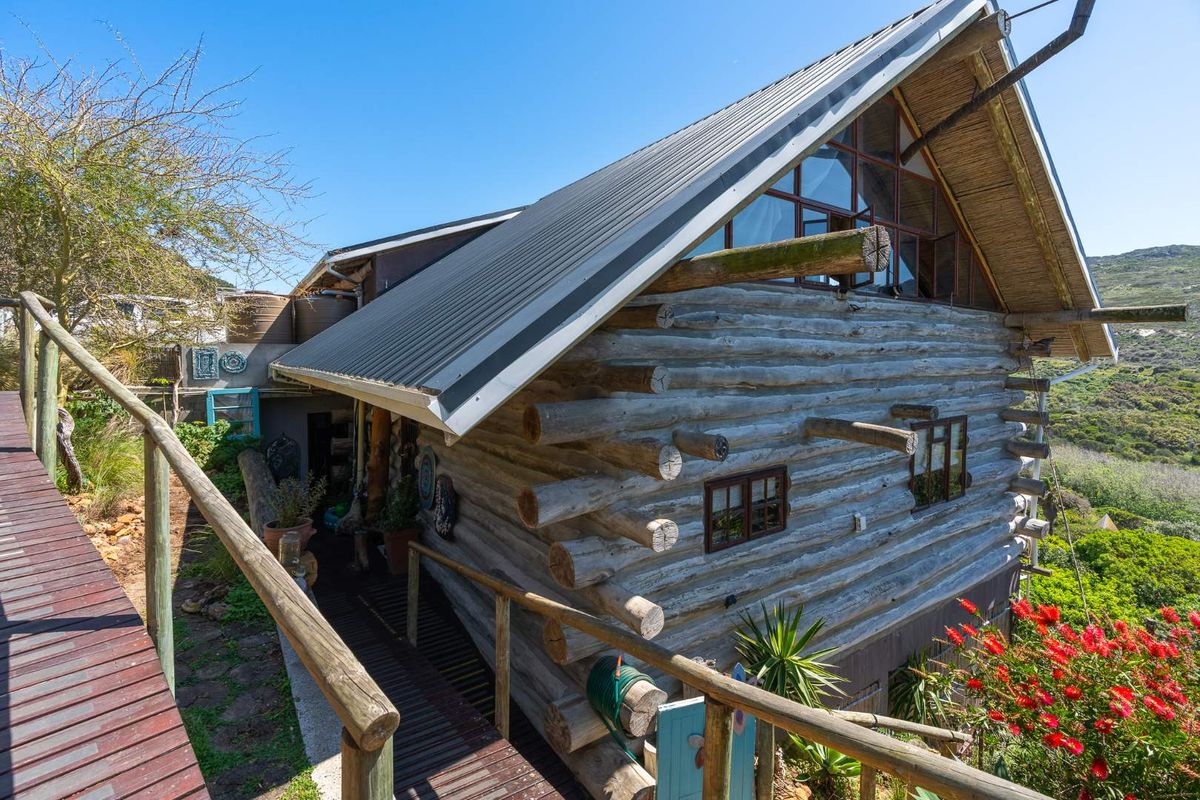Rear view of a rustic log cabin featuring a metal roof, elevated timber decking, and surrounding natural landscape.