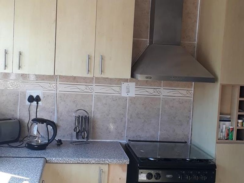 A functional kitchen featuring light wood cabinetry, tiled backsplash, granite-look laminate countertops, and a stainless steel extractor fan above a freestanding stove.
