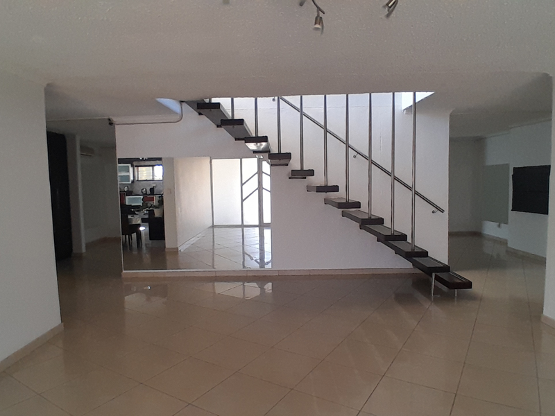 Spacious open-plan living area featuring a modern floating staircase with metal handrails and neutral tiled flooring throughout.