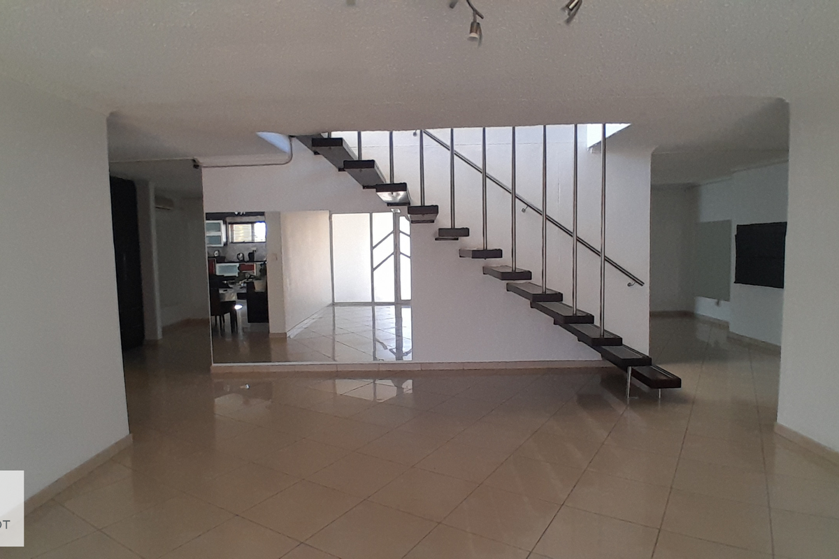 Spacious open-plan living area featuring a modern floating staircase with metal handrails and neutral tiled flooring throughout.
