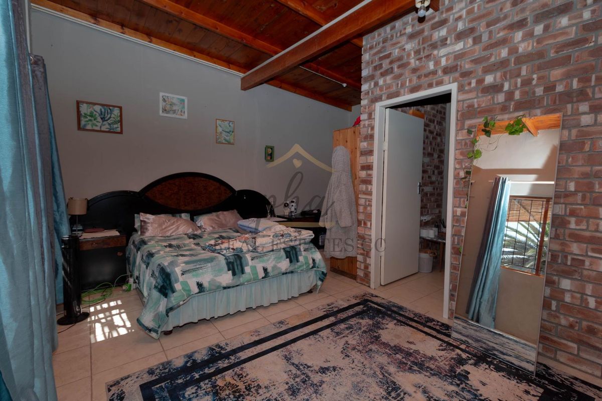 A bedroom featuring exposed timber ceiling beams and a rustic brick feature wall, with tiled flooring and an adjoining doorway.