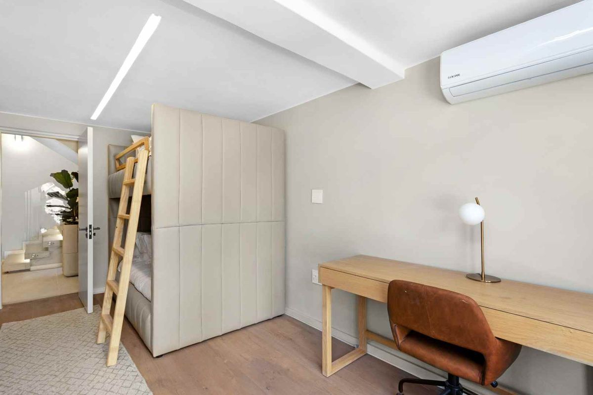 A modern bedroom featuring light wood flooring, a wall-mounted air conditioning unit, and a built-in bunk bed structure.