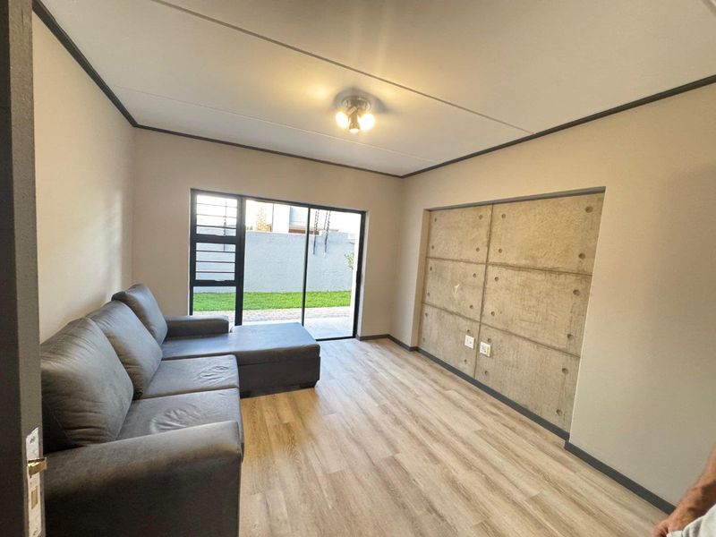 Modern living room featuring light laminate flooring, a striking exposed concrete feature wall, and a sliding glass door providing access to the outdoor area.