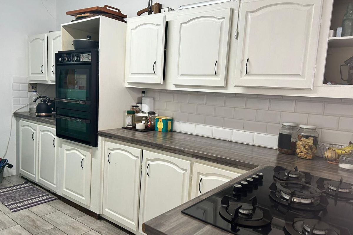 A functional kitchen featuring white cabinetry, a built-in double oven, a gas hob, and subway tile backsplash with wood-look laminate countertops.