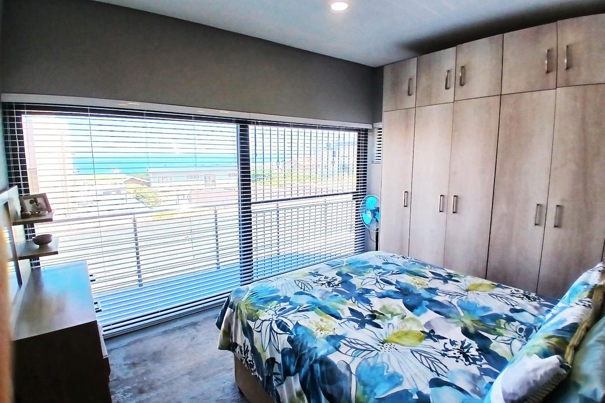 A well-lit bedroom featuring extensive built-in cabinetry and large windows with horizontal blinds, offering a view of the surrounding area.