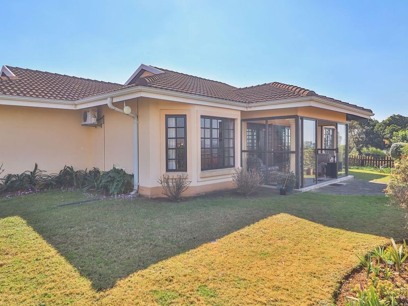 Rear view of the townhouse featuring a well-maintained lawn, tiled roof, and an enclosed patio area with sliding glass doors.