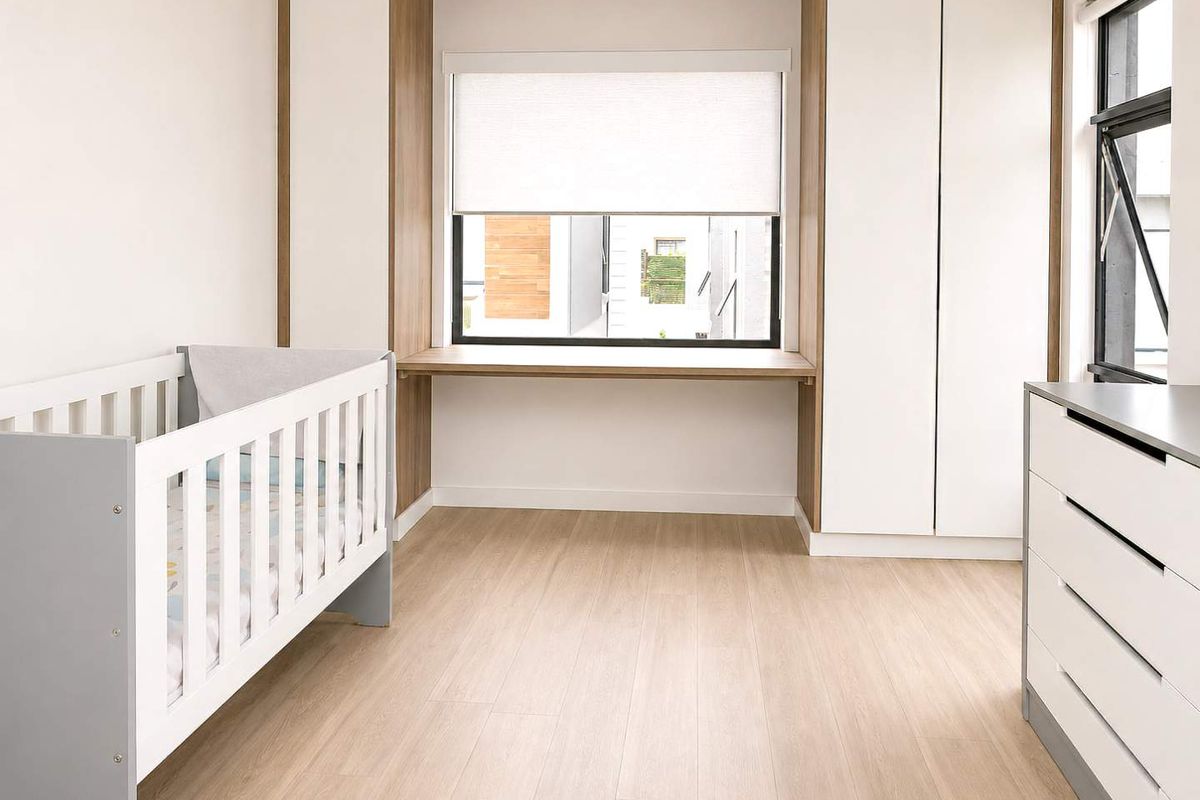 A bright, modern bedroom featuring built-in cabinetry, a recessed window nook with a desk, and light wood-look flooring.
