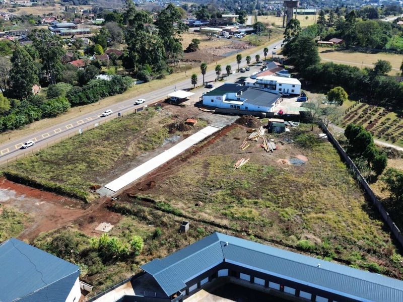 Aerial view of a vacant commercial land plot featuring a concrete driveway, perimeter fencing, and surrounding established commercial infrastructure.