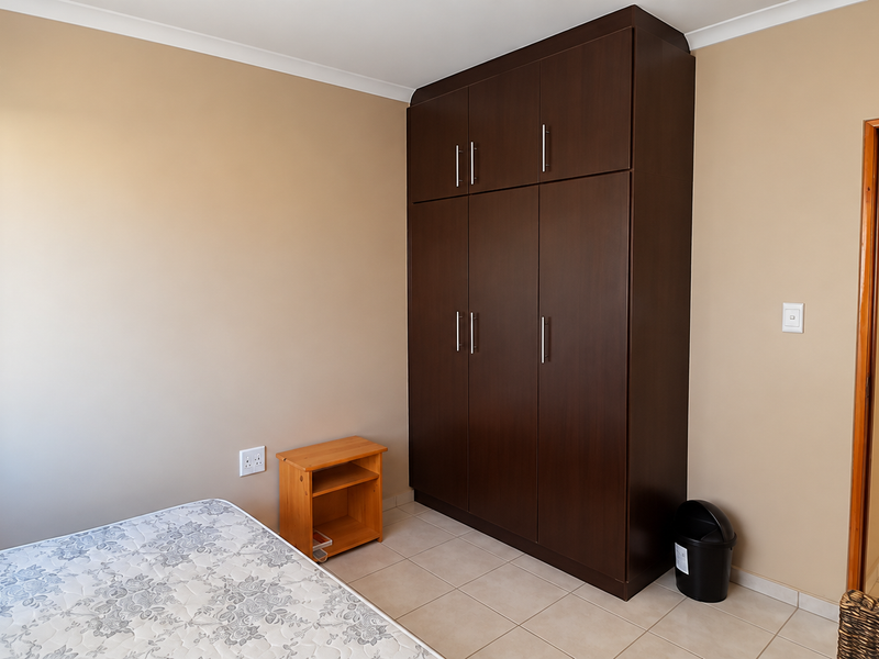 A bedroom featuring neutral wall tones, tiled flooring, and a dark wood built-in wardrobe providing ample storage space.