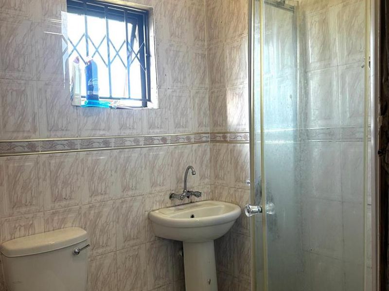 A compact bathroom featuring a pedestal basin, toilet, and a glass shower enclosure with full-height wall tiling.