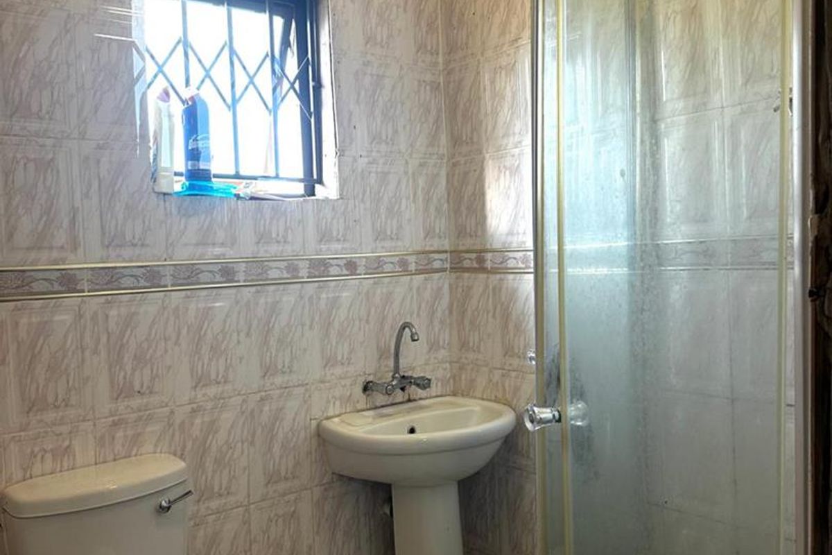 A compact bathroom featuring a pedestal basin, toilet, and a glass shower enclosure with full-height wall tiling.