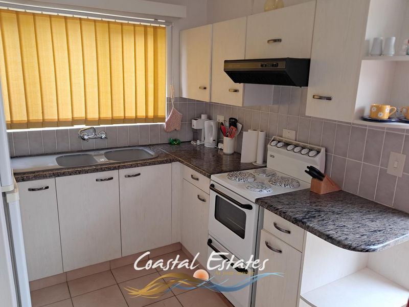 A functional kitchen featuring laminate cabinetry, granite-look countertops, a stainless steel double sink, and a freestanding electric stove with an extractor fan.