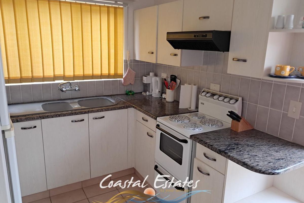 A functional kitchen featuring laminate cabinetry, granite-look countertops, a stainless steel double sink, and a freestanding electric stove with an extractor fan.