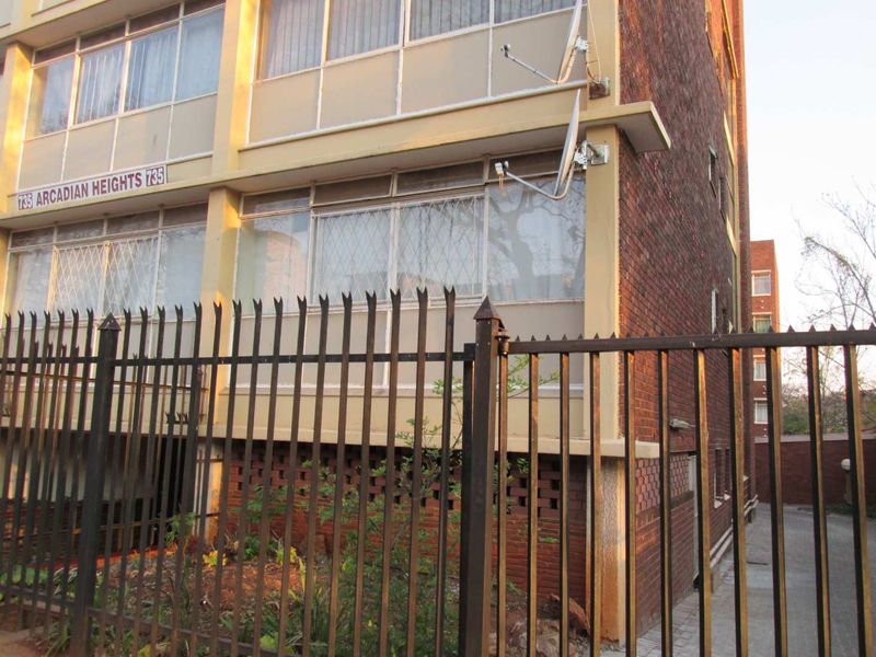 Exterior view of the Arcadian Heights apartment building, featuring a brick facade, security fencing, and window security bars.