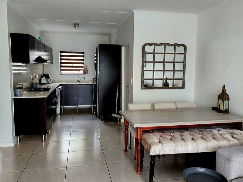 An open-plan living and dining area featuring a modern kitchen with dark cabinetry, gas hob, and tiled flooring throughout.