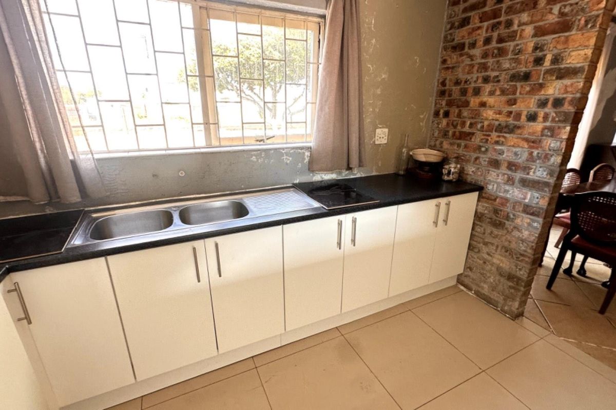 Kitchen area featuring white cabinetry, double bowl sink, built-in hob, and an exposed brick feature wall, requiring cosmetic wall repairs.