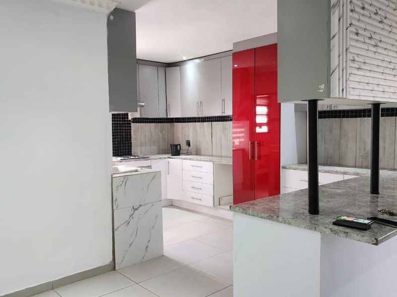 Modern kitchen featuring high-gloss red and white cabinetry, stone countertops, a breakfast bar, and tiled backsplash with neutral floor tiles.