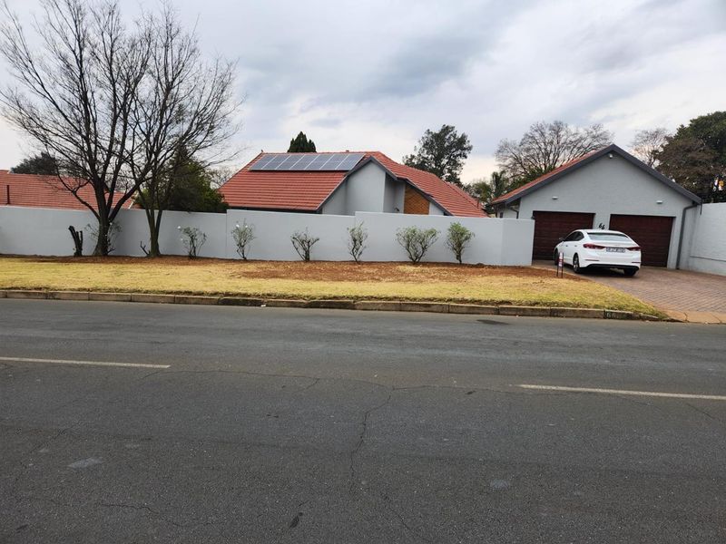 Front view of a residential property featuring a tiled roof with solar panels, a secure perimeter wall, and a double garage with a paved driveway.