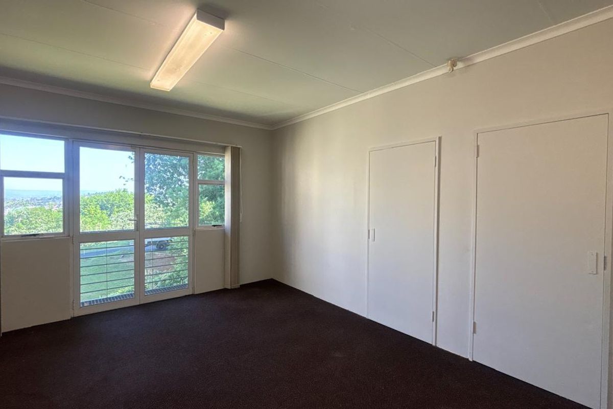 A bright, empty office space featuring neutral walls, carpeted flooring, built-in storage cupboards, and a large glass sliding door with natural light.